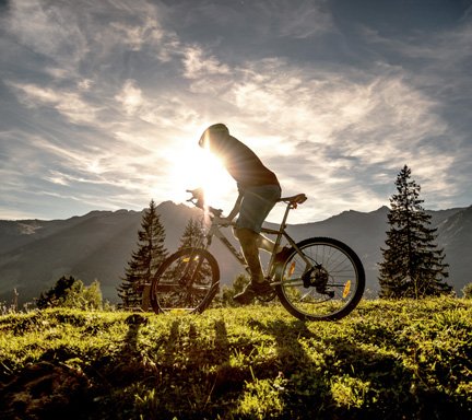 Mountainbiker unterwegs in den Bergen. Die Sonne geht im Hintergrund unter, der Biker wirft einen Schatten. Er ist auf einem Trail in Gastein unterwegs.